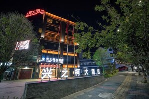A multi-story hotel with illuminated signage, a brick facade, and a paved walkway. - Xingzhike Hotel (Wuchuan)