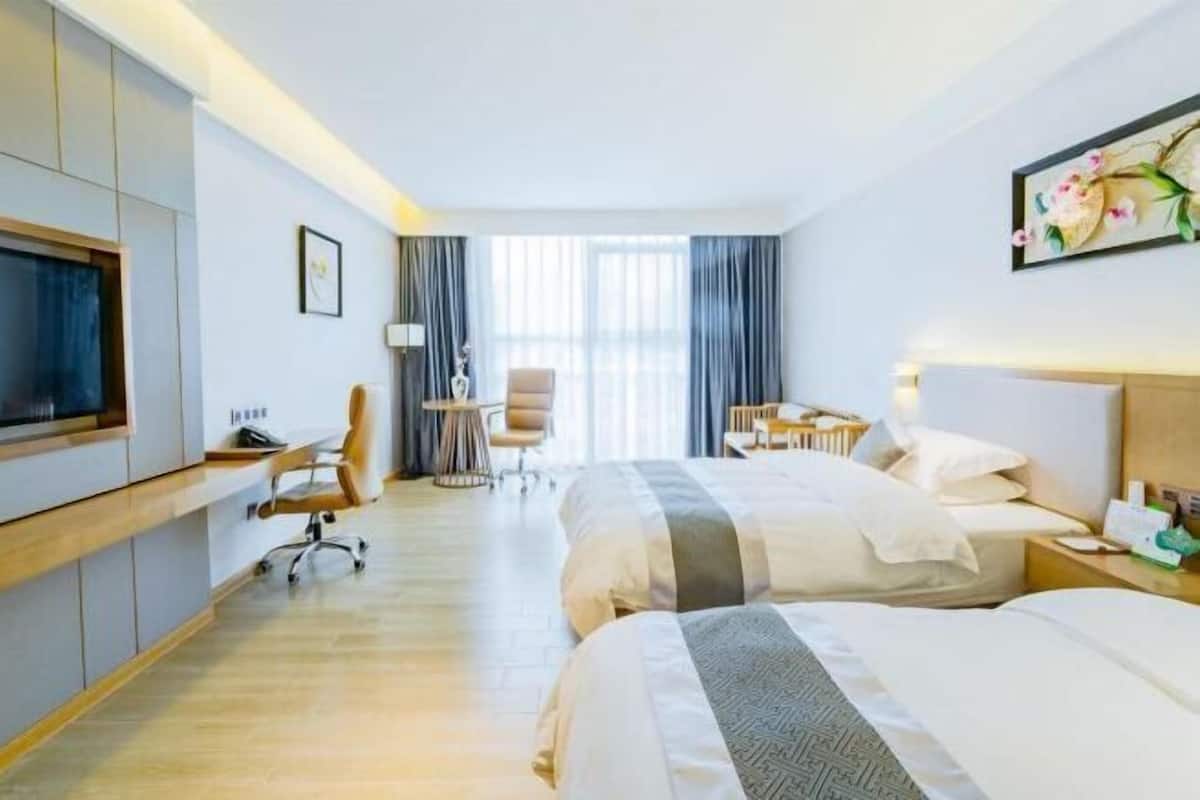 A hotel room with two beds, a desk, a chair, a TV, and a large window with curtains.