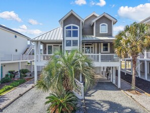 A two-story house with a covered porch, a garage, and a small garden with palm trees.