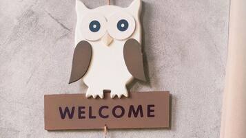 Een houten uil decoratie met een 'WELCOME' bordje aan een ruwe muur.