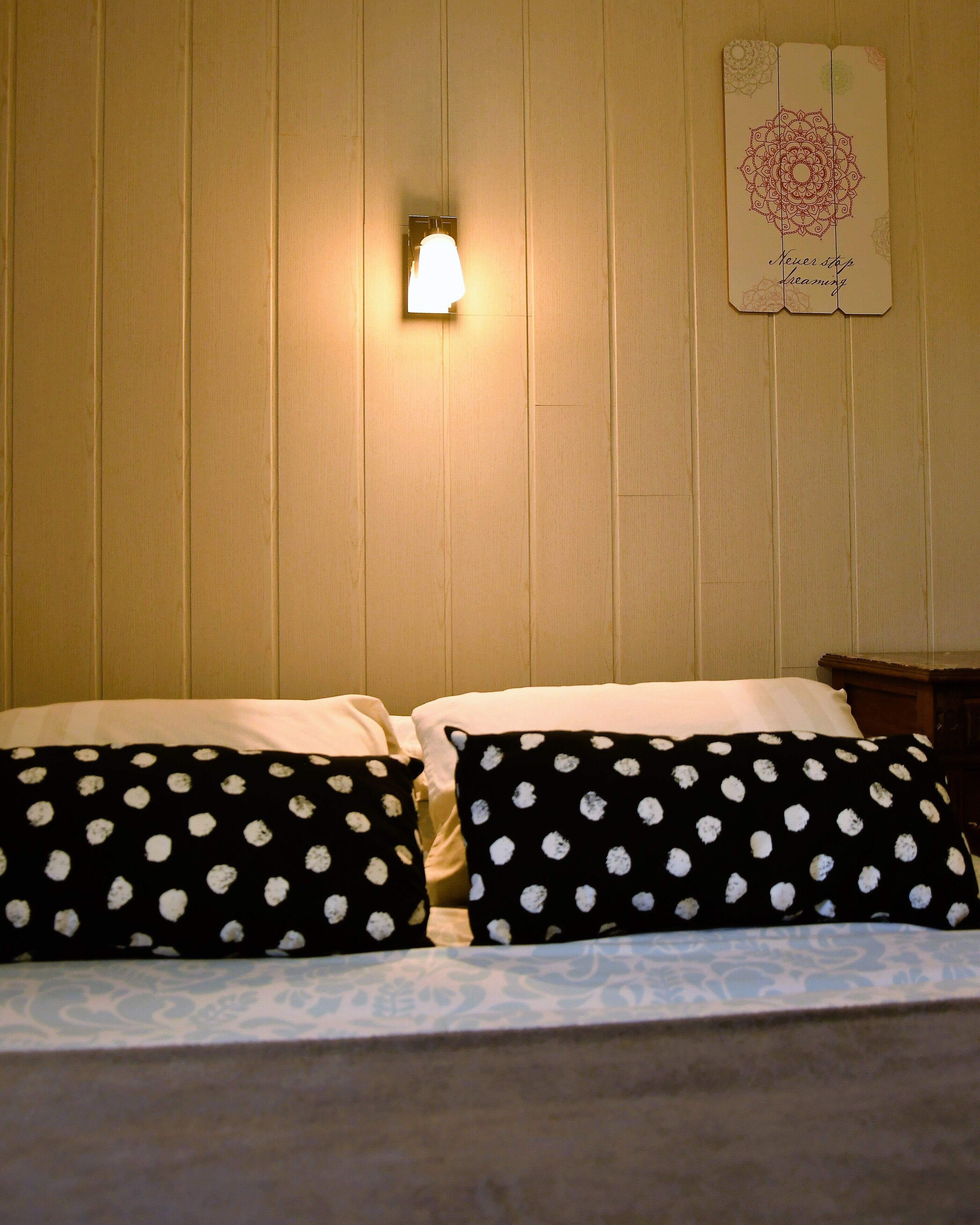 A bed with black pillows with white polka dots, a wall-mounted light, and a framed picture with a mandala design.