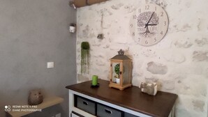 A room with a rustic stone wall, a wooden dresser, a green candle, a lantern, and a wall clock with a tree design.