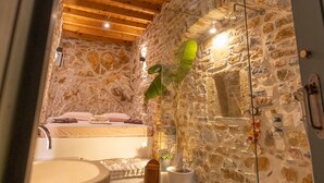 Une salle de bain aux murs en pierre, équipée d’une baignoire, d’un lavabo et d’un espace douche.