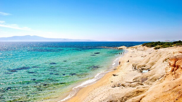 Une plage à l’eau turquoise et limpide, bordée d’un rivage sablonneux, avec des montagnes qui se dessinent à l’horizon.