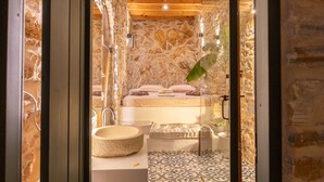 Une salle de bain aux murs en pierre, dotée d’une baignoire, d’un lavabo et d’un sol à motifs.
