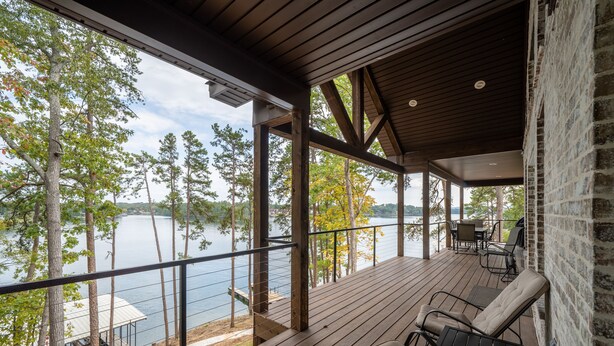 Une terrasse en bois offrant une vue sur un lac, des meubles d’extérieur et un mur en briques.