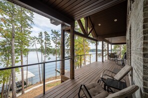 A wooden deck with a view of a lake, outdoor furniture, and a brick wall. - New Hot Springs Lakehouse with Double Stall Dock & Boat for Rent! (Hot Springs)