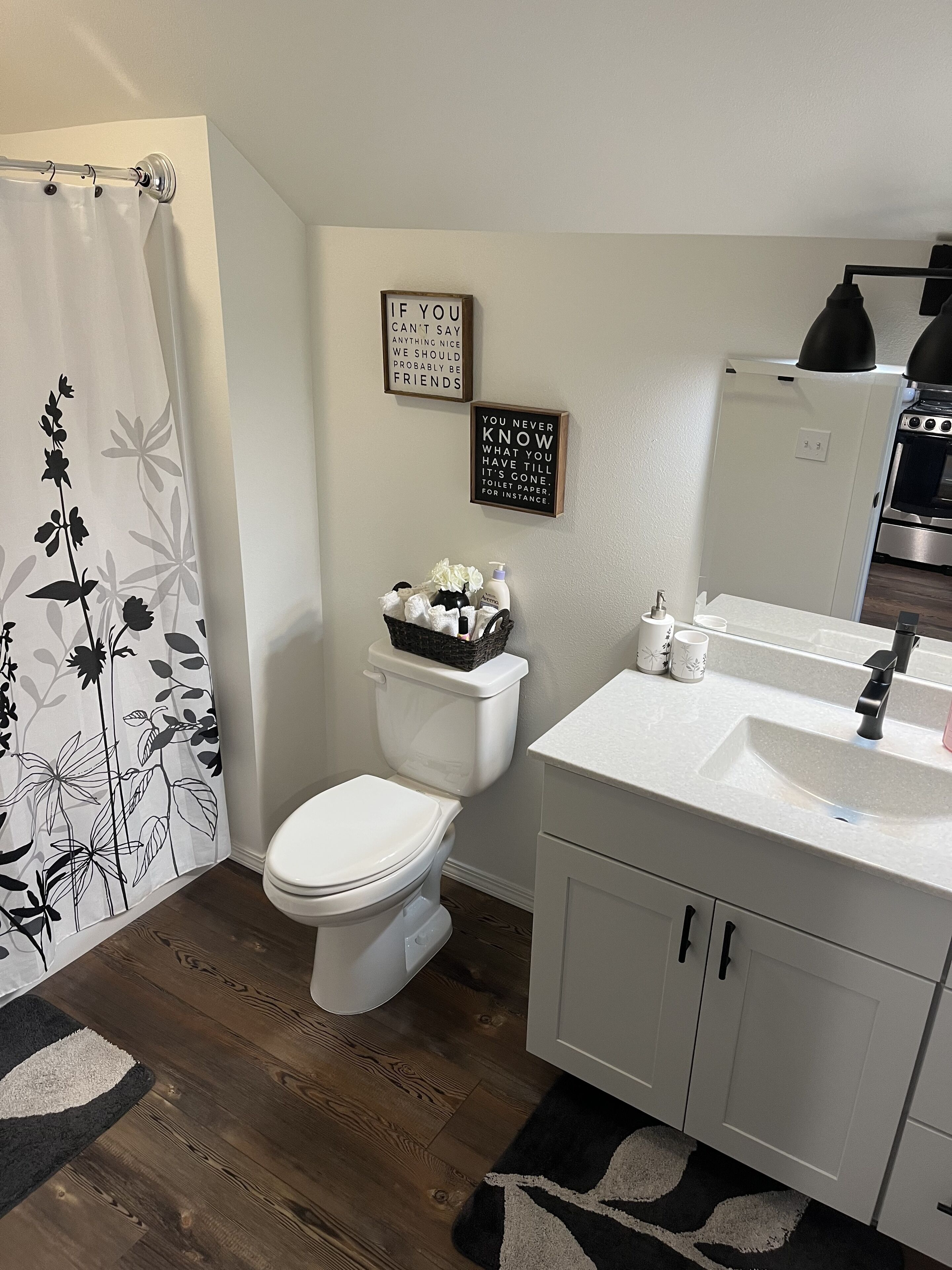 Une salle de bain avec des toilettes, un lavabo et un rideau de douche. Deux panneaux avec du texte sont fixés au mur.