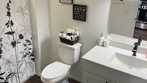 Ein Badezimmer mit Toilette, Waschbecken und Duschvorhang. An der Wand befinden sich zwei Schilder.