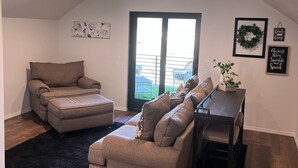 Ein geräumiges Wohnzimmer mit einem großen, grauen Ecksofa, einem Esstisch mit Stühlen und einem schwarzen Teppich. Ein Glastür ermöglicht den Zugang zu einem Balkon.