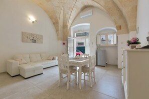Un espacio habitable amplio con un sofá blanco, una mesa de comedor con sillas y una cocina al fondo.