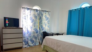 Ein Schlafzimmer mit Bett, Kommode, Fernseher und Vorhängen.