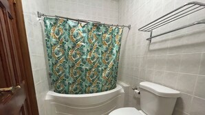 Ein Badezimmer mit einer weißen Toilette, einer Badewanne mit einer Duschvorhang mit Blättermotiv und einem Handtuchhalter über der Toilette.