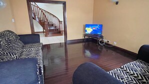 Ein Wohnzimmer mit einer Holztreppe, einem Fernseher und gemusterten Sofas.