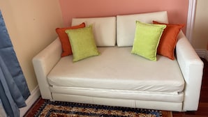 Um sofá de couro branco com três almofadas em um quarto com um tapete estampado e parede rosa.