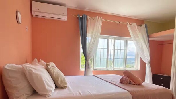 Quarto com cama, roupa de cama branca, janela com cortinas, ar condicionado e mesa de cabeceira.