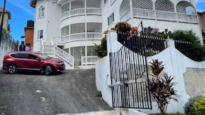 Um edifício de vários andares com fachada curva, entrada com portão e um carro vermelho estacionado na frente.