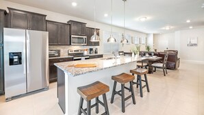 A modern kitchen with dark cabinets, stainless steel appliances, a granite countertop, and bar stools.