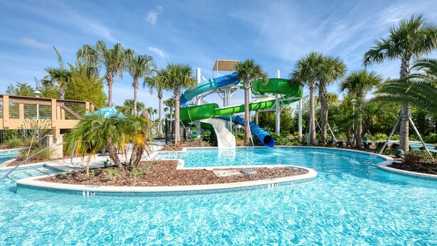 A swimming pool with a water slide, palm trees, and a clear blue sky.