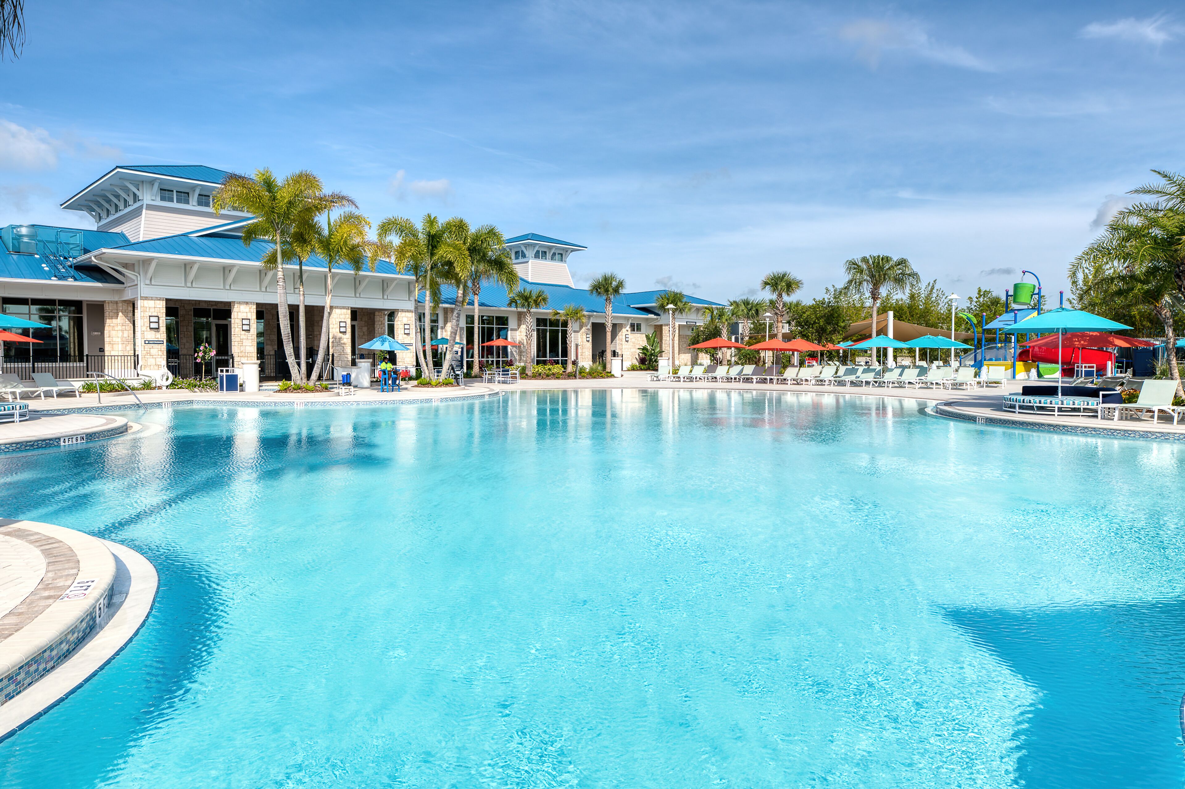 Een groot zwembad met een modern hotel op de achtergrond, inclusief terrasjes en palmbomen.