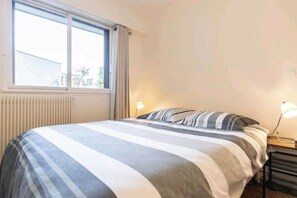 Une chambre à coucher avec un lit, une fenêtre, un radiateur et une table de chevet avec une lampe.