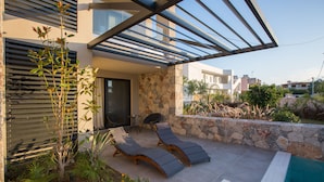 Zona de piscina exterior moderna amb gandules, un mur de pedra i vista als edificis veïnals.