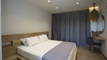 A bedroom with a wooden headboard, a bed with white bedding, a desk with a chair, and a large window with curtains.