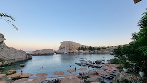 Un hotel a la vora d'una platja, amb gandules, ombrel·les i una costa rocosa.