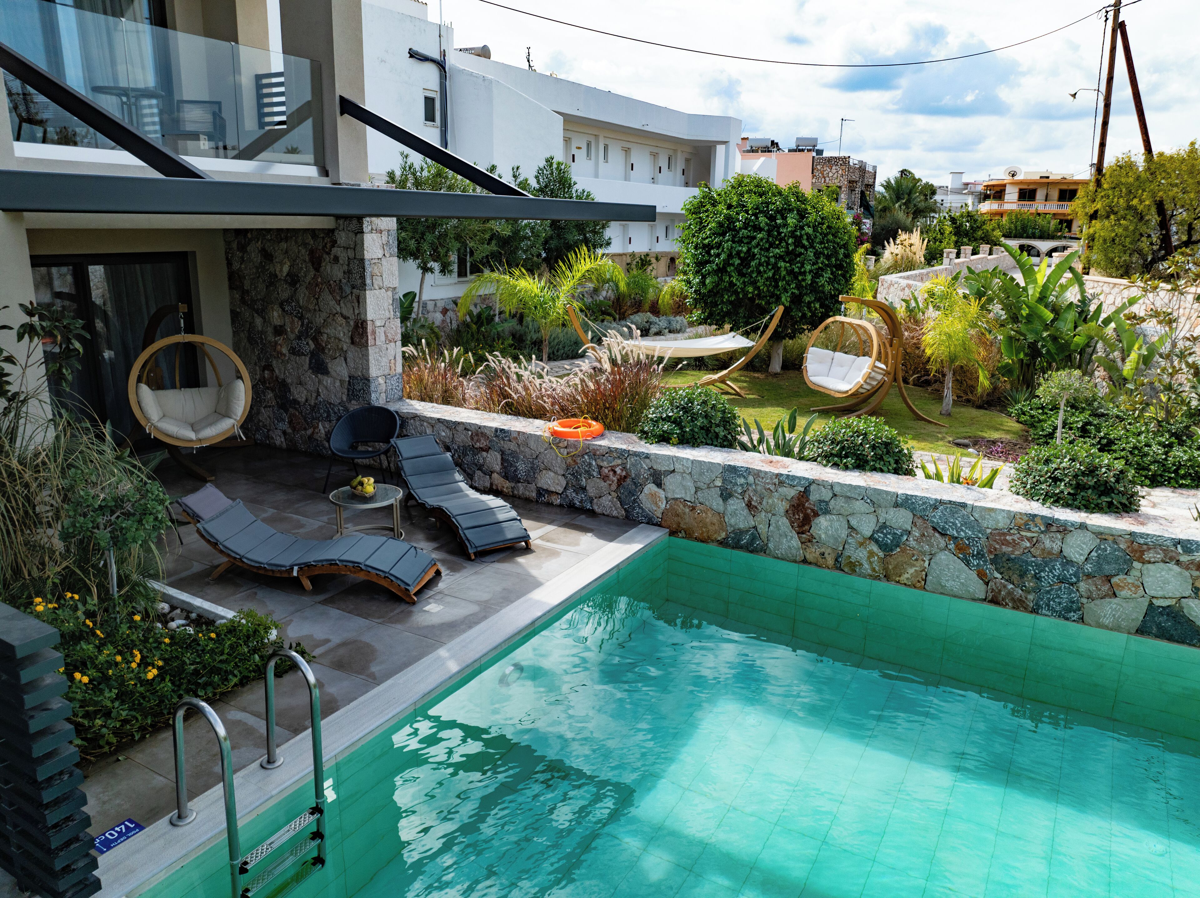 Un área de piscina moderna al aire libre con sillones de descanso y un muro de piedra.