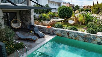 Un área de piscina moderna al aire libre con sillones de descanso y un muro de piedra.