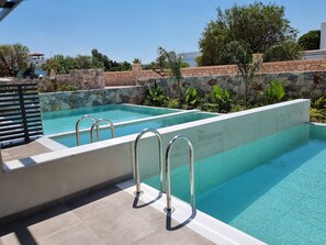 A swimming pool with two metal ladders, surrounded by stone walls and greenery. - DeLight Luxury Rooms (Rhodes)