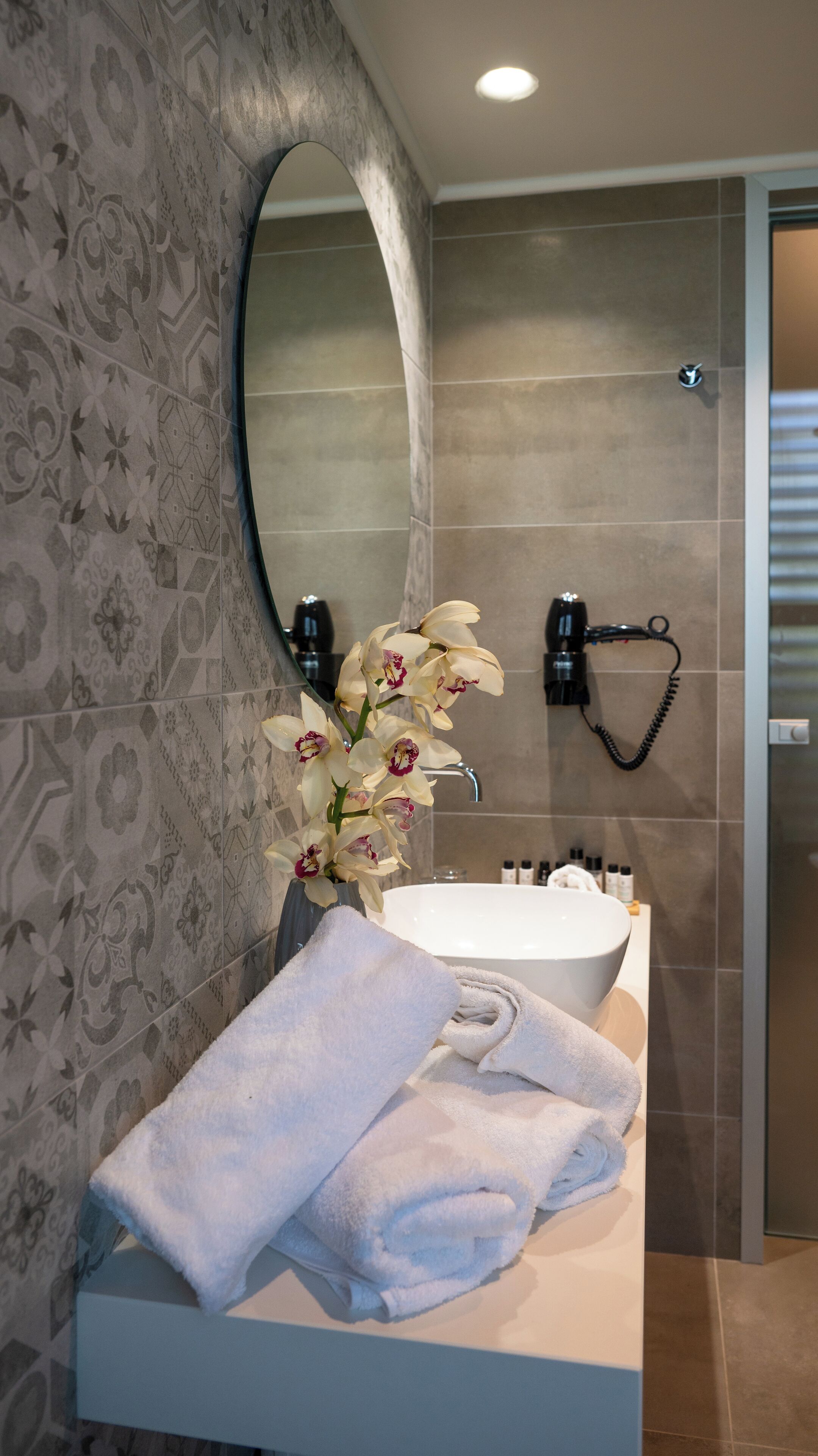 A bathroom with a white sink, a mirror, a towel, and a vase with flowers.