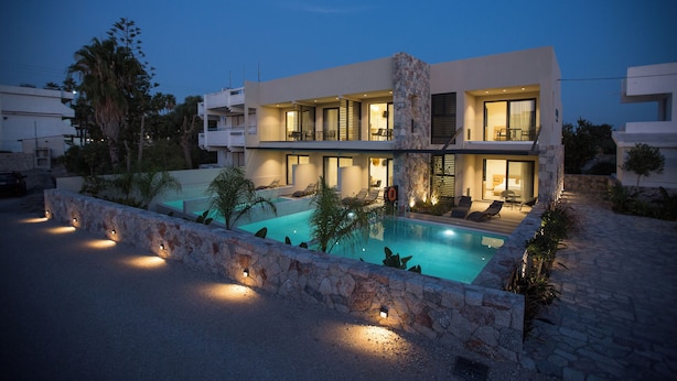 Una casa moderna de dos pisos amb piscina, parets de pedra i mobiliari exterior.