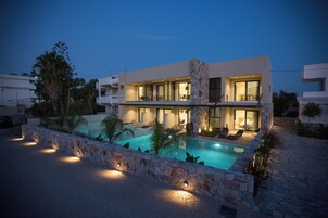 A modern two-story house with a swimming pool, stone walls, and outdoor seating.