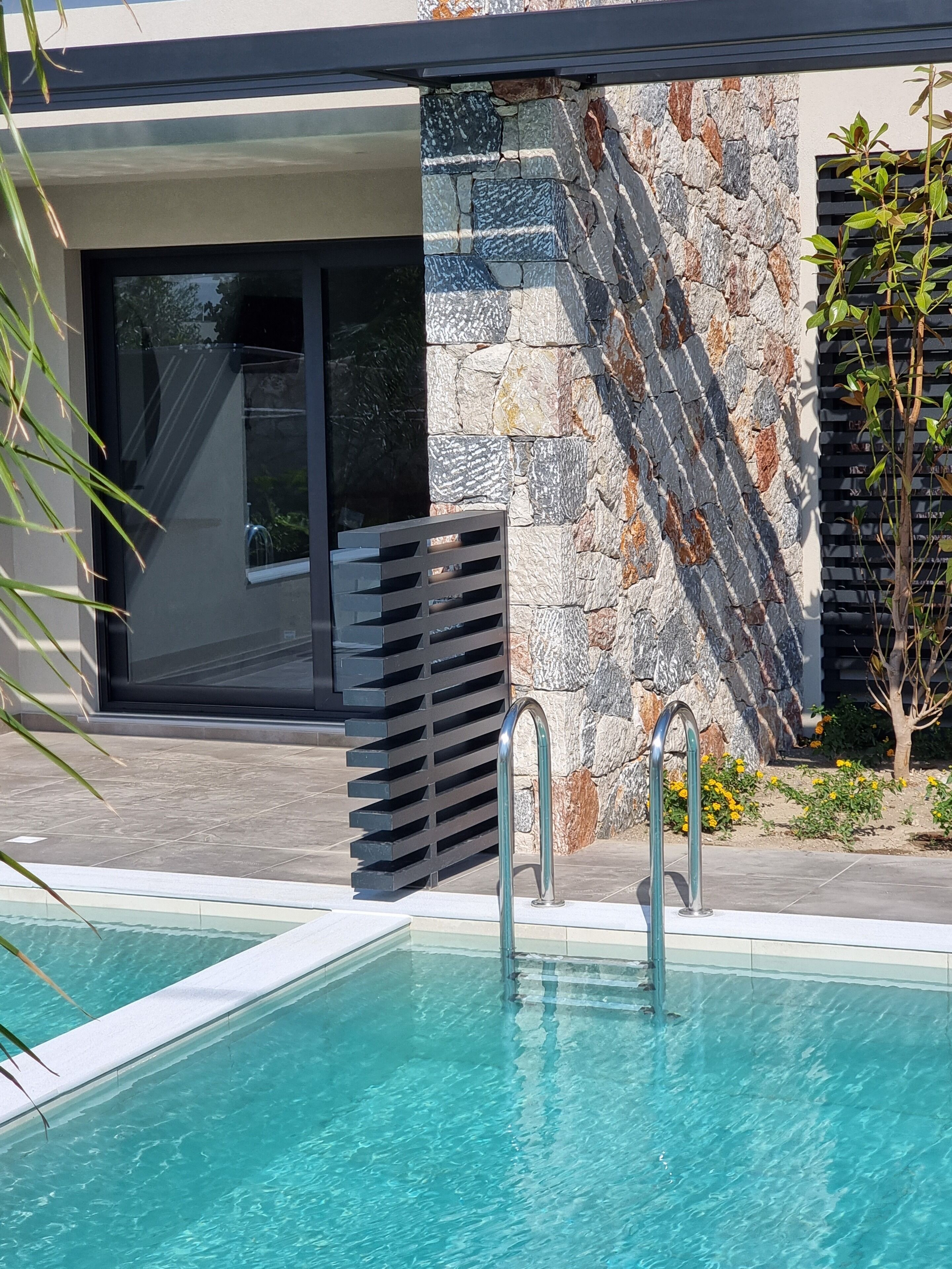 Un área de piscina moderna al aire libre, con un muro de piedra y una cerca de metal.