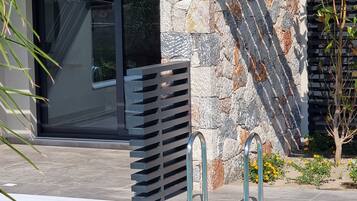 Un área de piscina moderna al aire libre, con un muro de piedra y una cerca de metal.