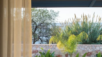 Un área junto a la piscina con dos sillones de madera, un muro de piedra y diversas plantas.