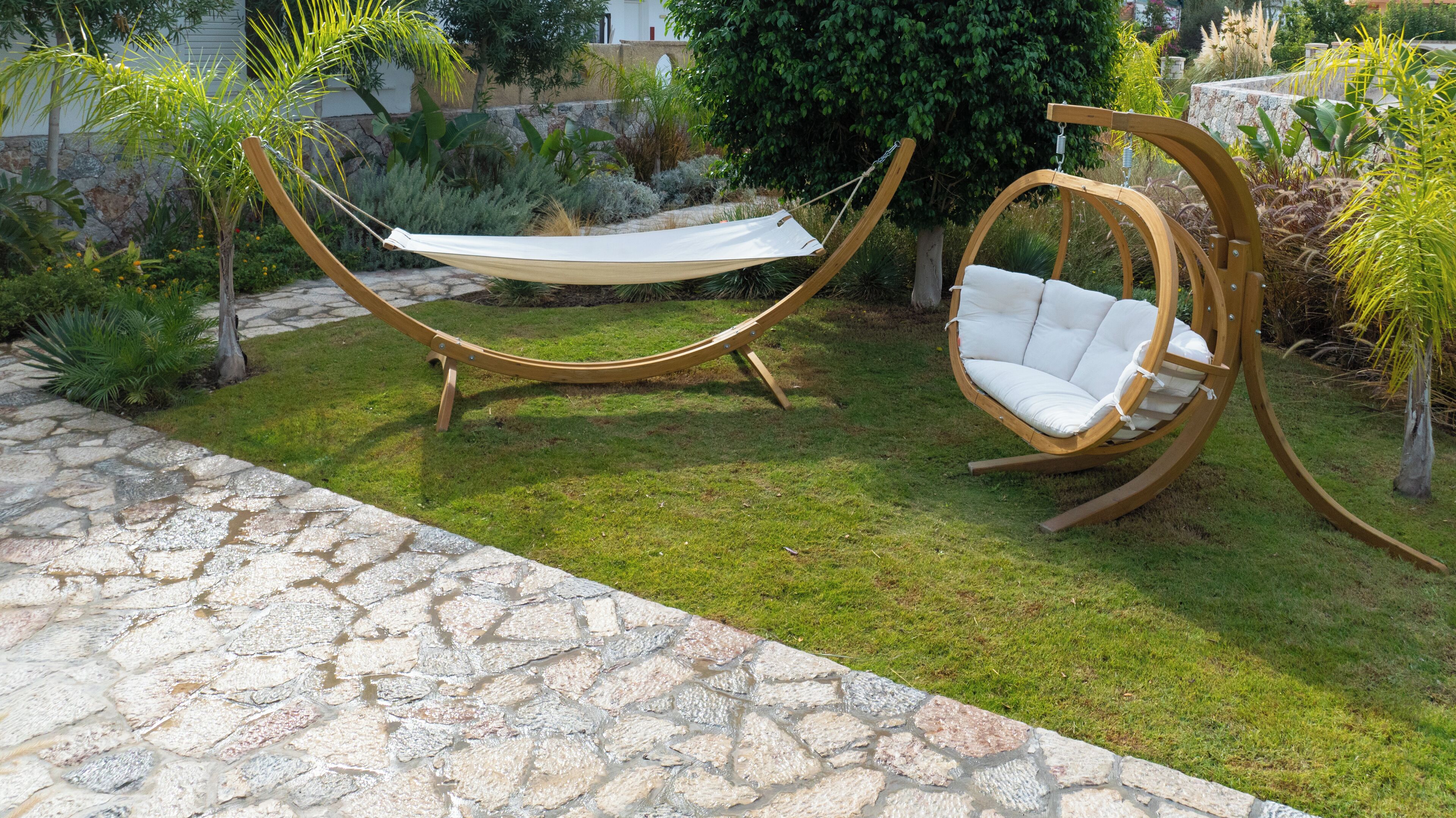 A hammock and a swing chair in a garden with stone flooring and various plants.