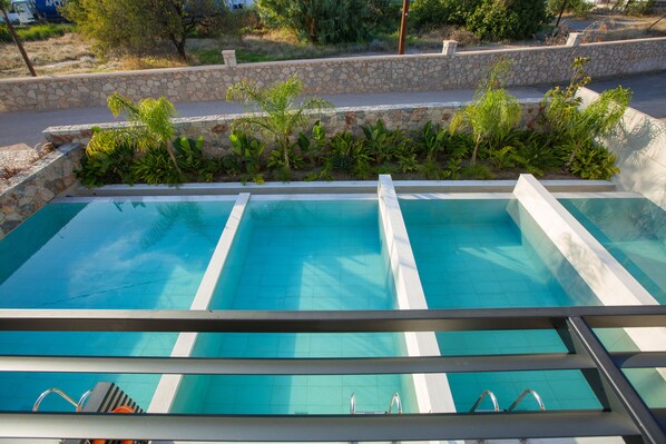 A swimming pool with clear blue water, surrounded by a stone wall and lush greenery. - DeLight Luxury Rooms (Rhodes)