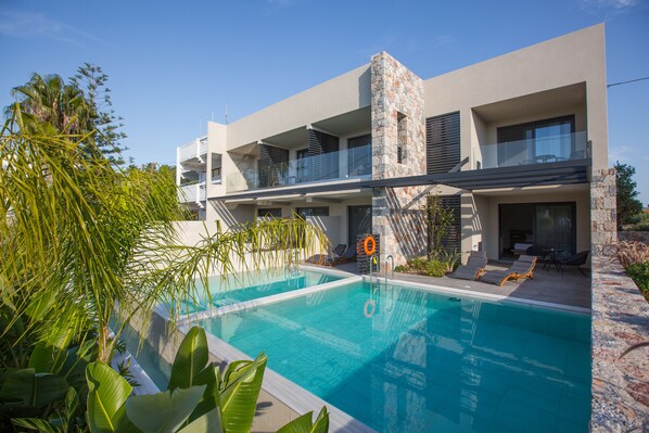 A modern building with a swimming pool, outdoor seating, and a stone accent wall. - DeLight Luxury Rooms (Rhodes)