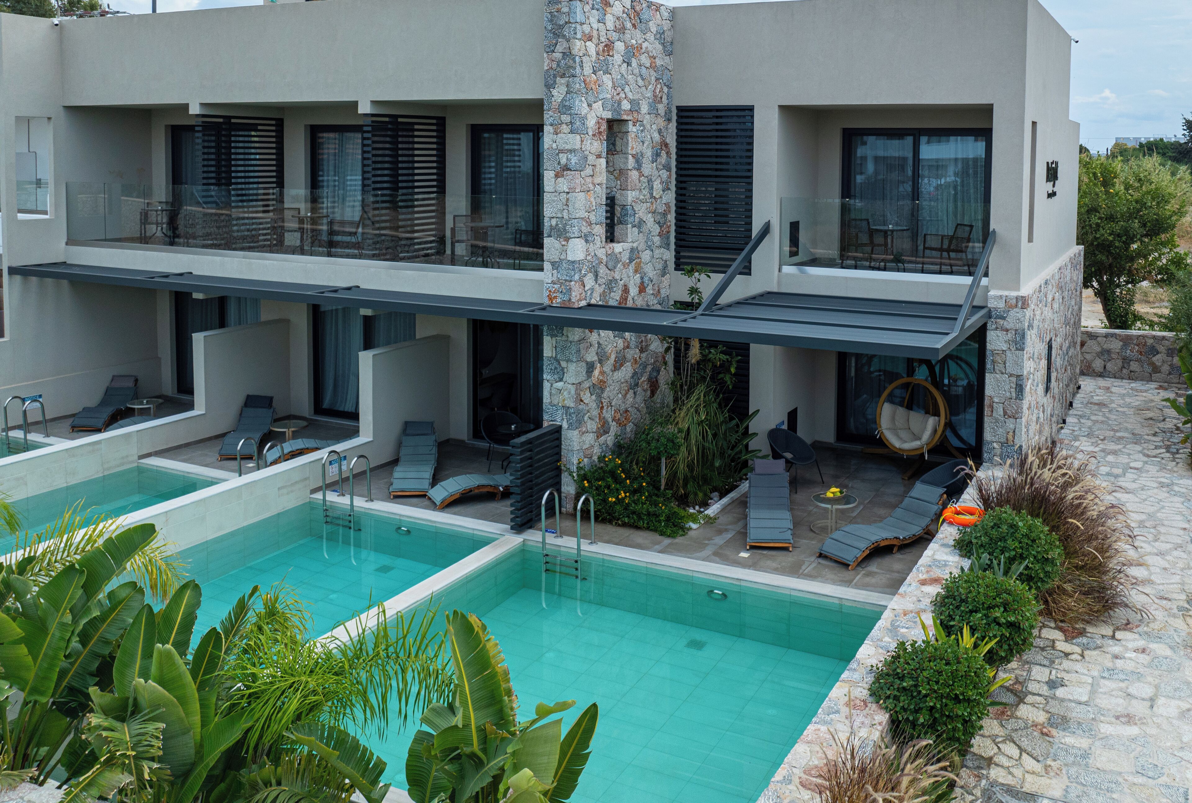 Un edificio moderno con un área de piscina, que incluye dos piscinas, sillas de descanso y una zona de estar cubierta.