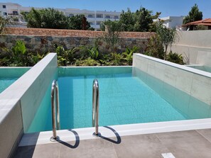 A swimming pool with stone walls and metal railings, surrounded by greenery and buildings in the background. - DeLight Luxury Rooms (Rhodes)