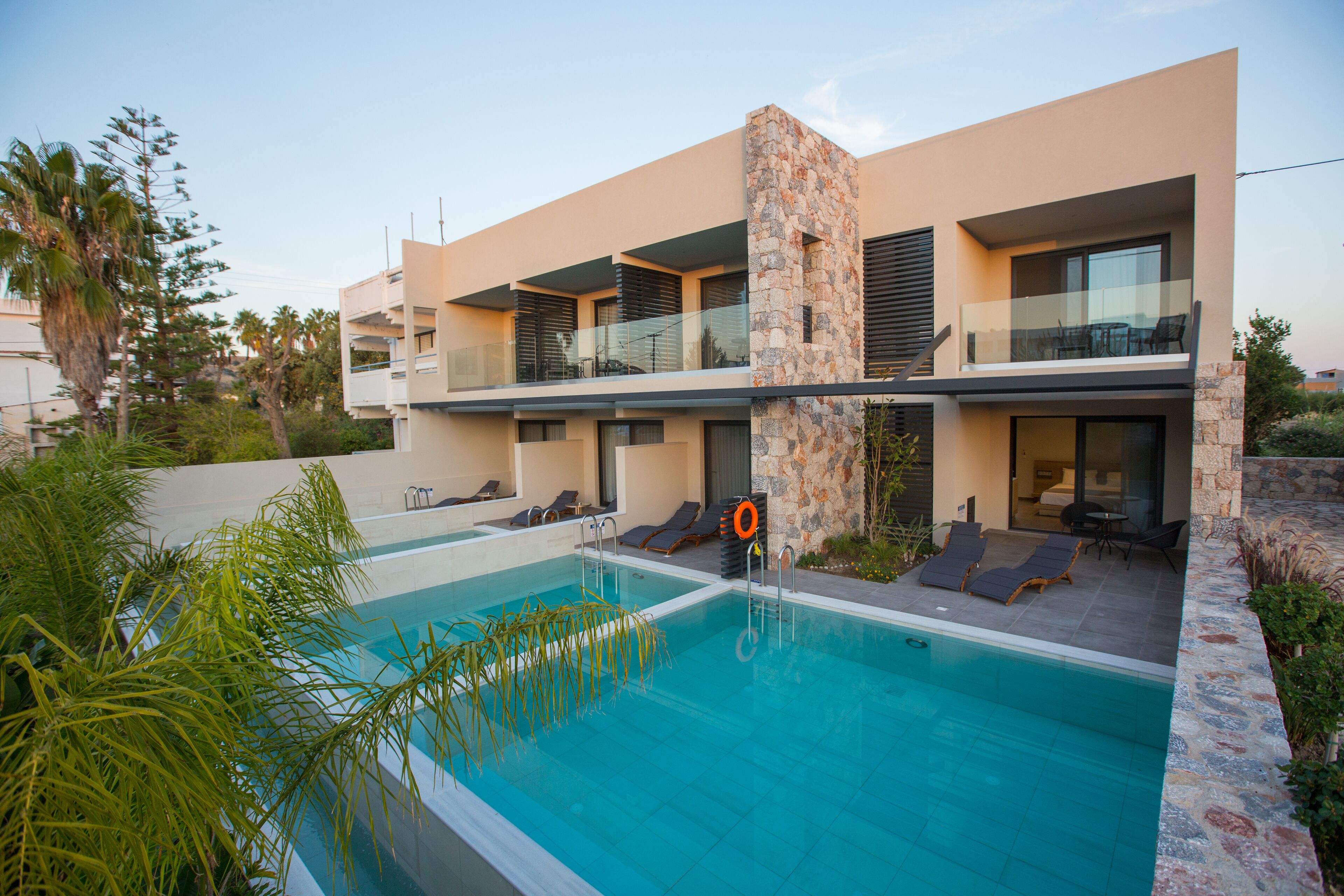 Un edificio moderno de dos pisos con piscina, mobiliario exterior y fachada de piedra.