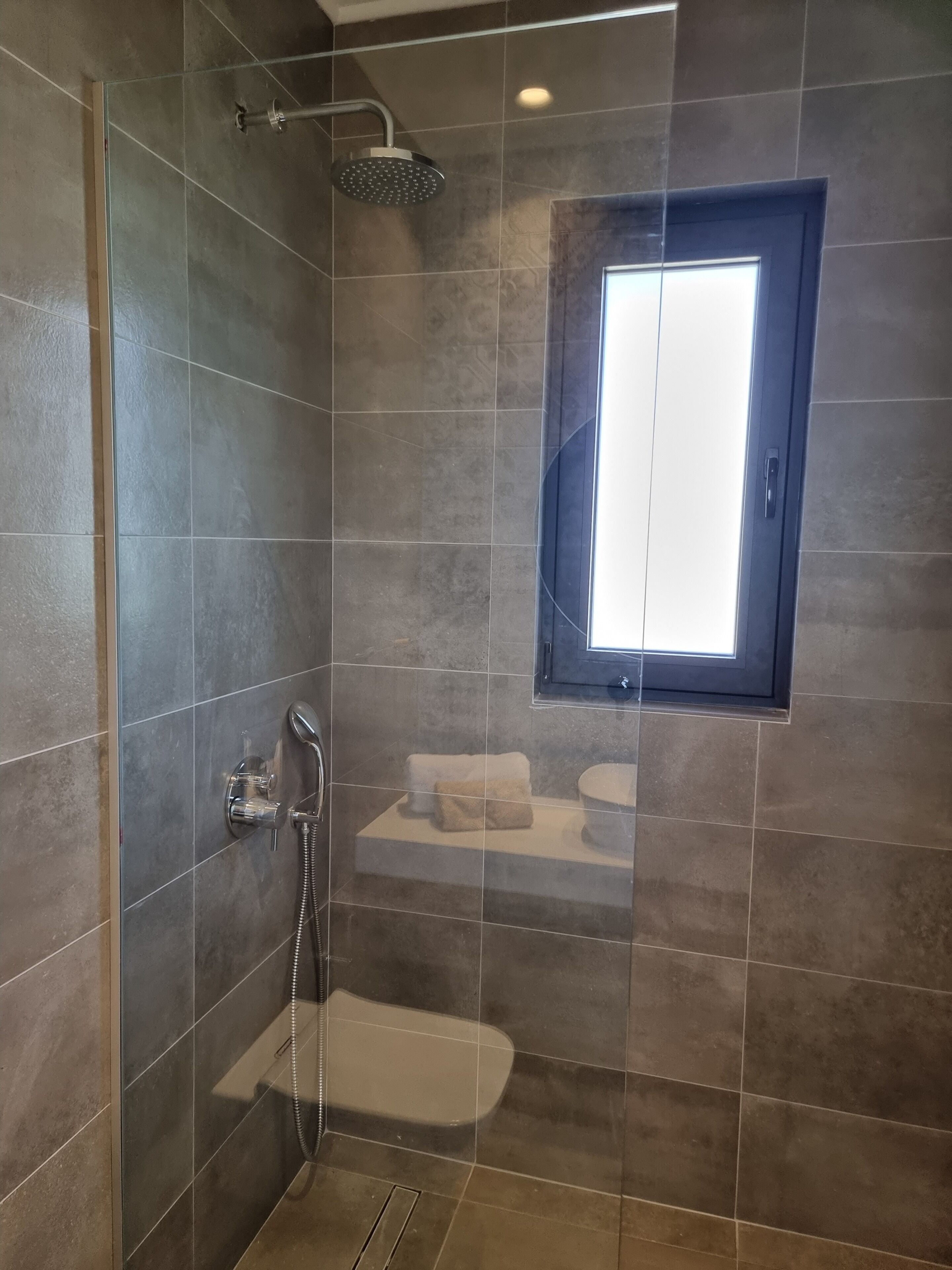 A modern bathroom with a shower, a toilet, and a small window.