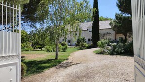 A gravel driveway leading to a stone building with a sloped roof, surrounded by greenery and a tall tree. - Chambre vue sur le Jardin (Rivière)