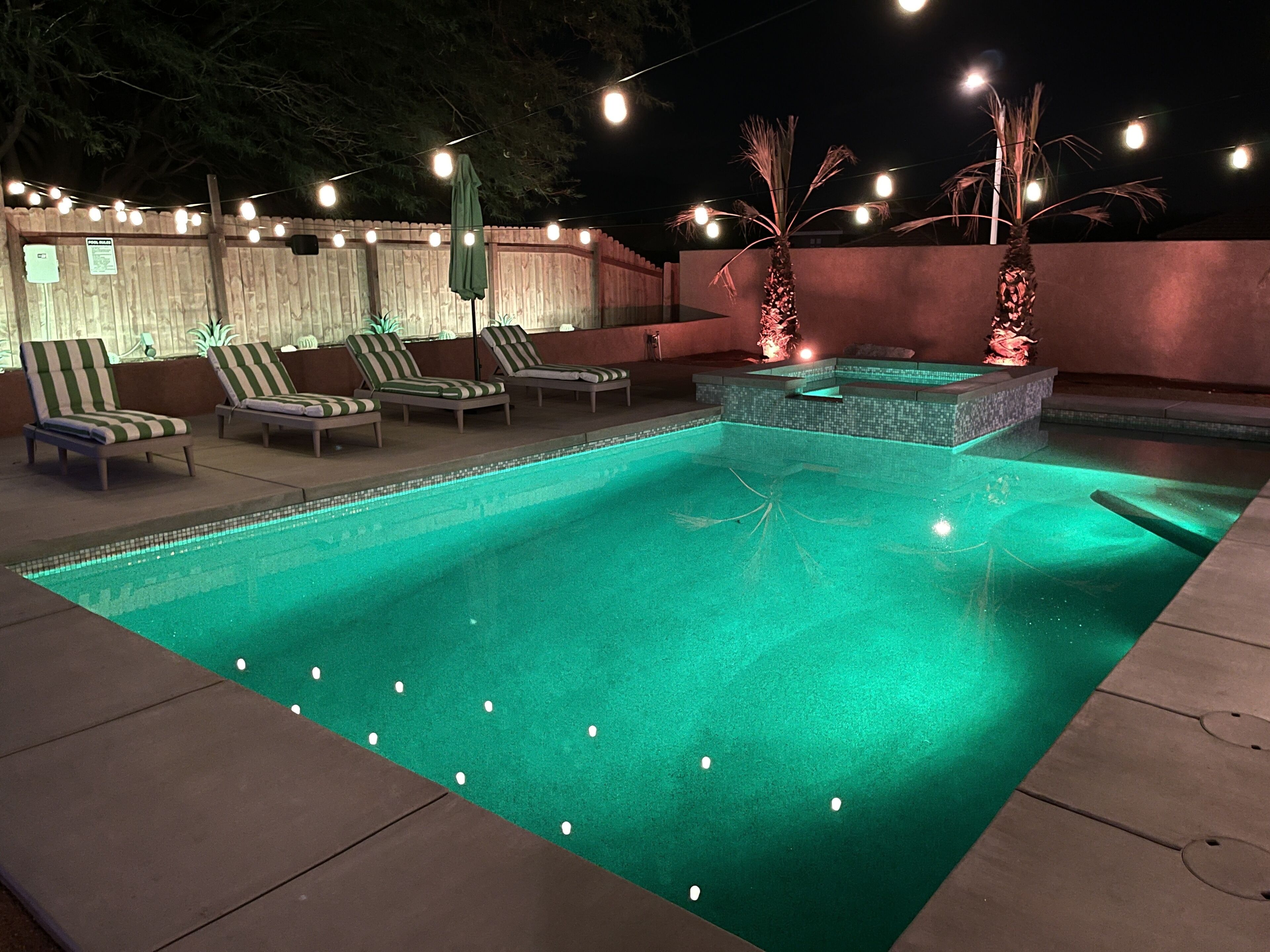 A nighttime outdoor pool area with lounge chairs and string lights.