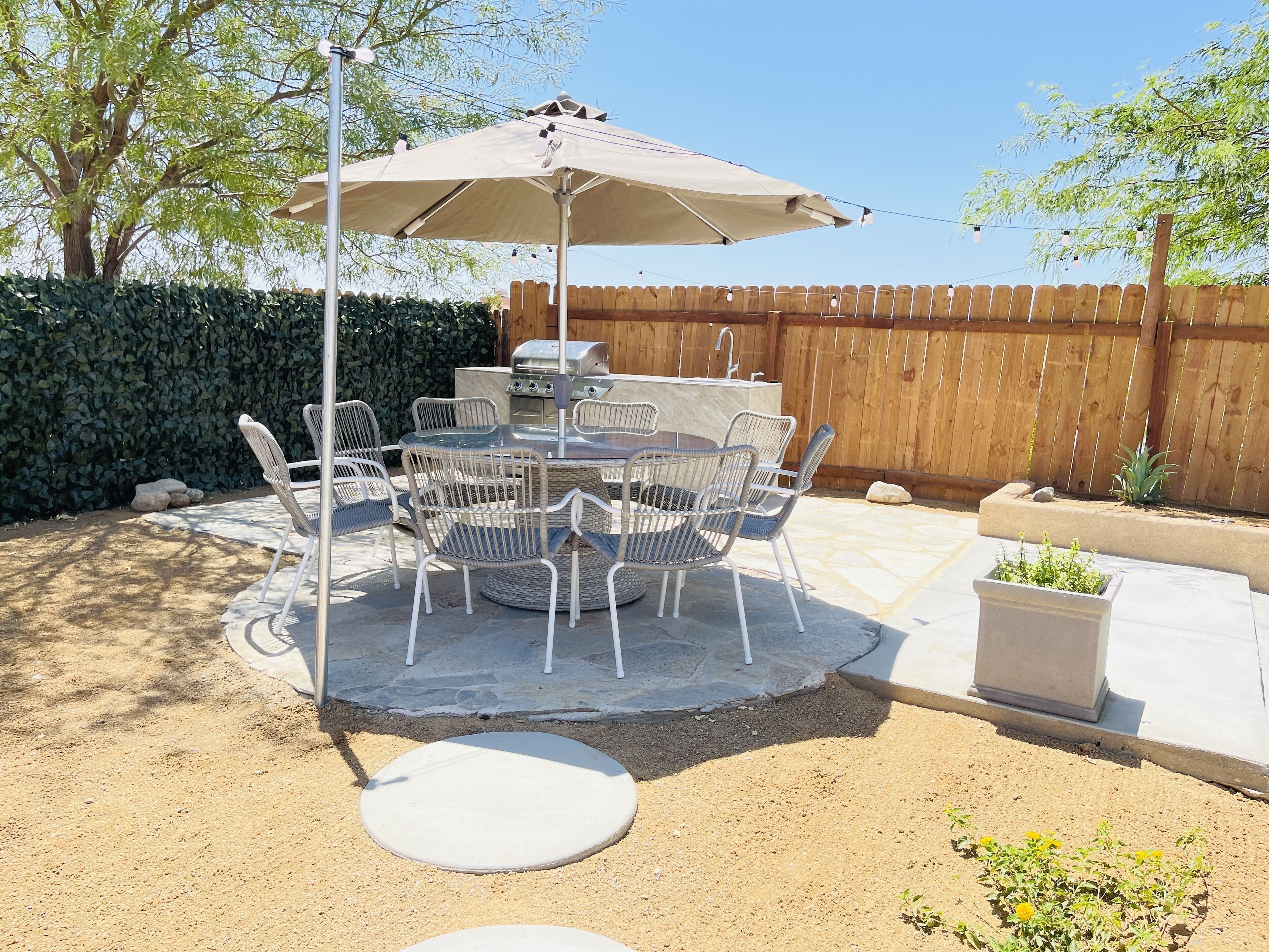 An outdoor patio with a round table and chairs, a grill, and a wooden fence.