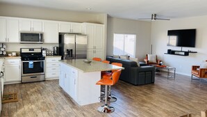 A modern kitchen with white cabinets, stainless steel appliances, and a central island with orange bar stools. - Beautiful Desert Retreat - Salt Water Pool & Spa (Desert Hot Springs)