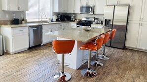 A modern kitchen with white cabinets, stainless steel appliances, and a central island with bar stools. - Beautiful Desert Retreat - Salt Water Pool & Spa (Desert Hot Springs)