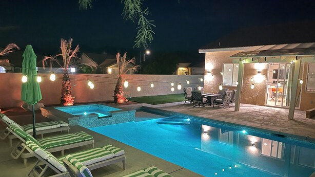A swimming pool with lounge chairs and string lights. - Beautiful Desert Retreat - Salt Water Pool & Spa (Desert Hot Springs)